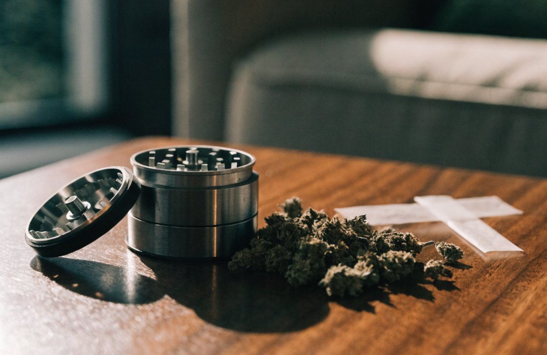 A metal grinder with dried cannabis flower and rolling papers - Bud Cargo