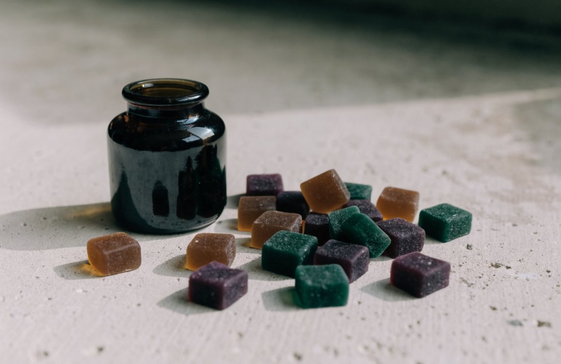 An assortment of THC gummies beside a dark glass jar - Bud Cargo