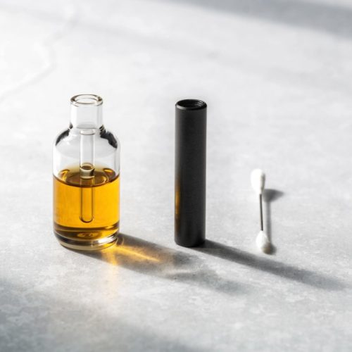 Glass 510 vape cartridge with amber oil next to a black vape battery and a cotton swab for cleaning the contacts